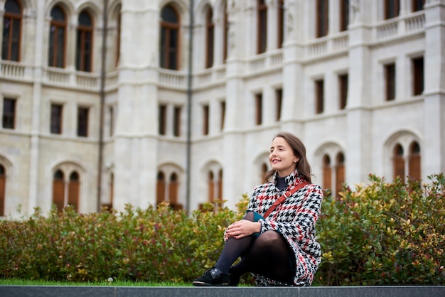 Mulher com um sorriso doce senta-se na grama verde no do Palácio do Parlamento em Budapeste