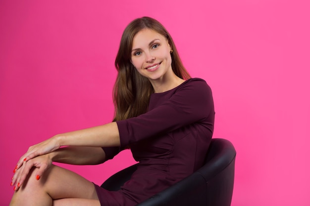 Mulher com um sorriso no rosto e cabelos soltos em uma parede rosa