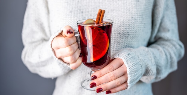 Mulher com um suéter branco quente segurando um copo de vinho quente nas mãos