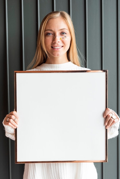 Mulher com um suéter branco segurando uma moldura de madeira