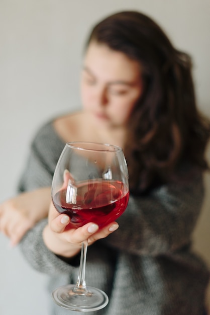 Mulher com um suéter cinza com uma taça de vinho tinto