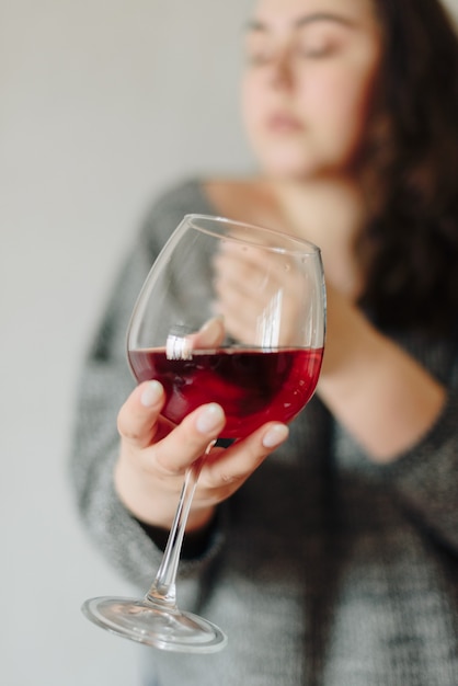 Mulher com um suéter cinza com uma taça de vinho tinto