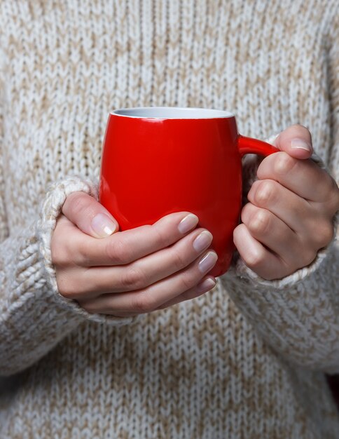 Mulher com um suéter leve segurando uma xícara vermelha de café.