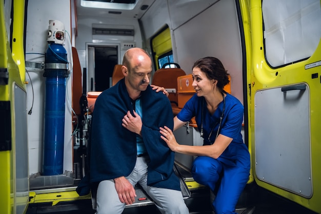 Mulher com um uniforme médico, falando amigavelmente e sorrindo para um homem ferido em um cobertor.