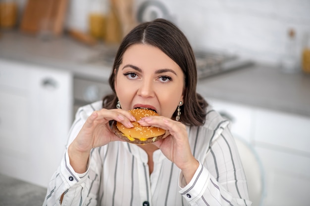 Mulher com uma blusa listrada comendo um hambúrguer grande