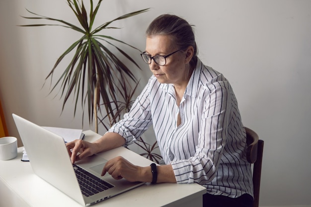 Mulher com uma camisa listrada branca envelhecida sentada em um computador em casa