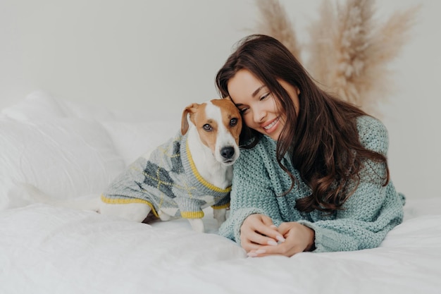Mulher com uma camisola aconchegante abraçando seu cão na cama compartilhando um momento de afeto confortável e feliz