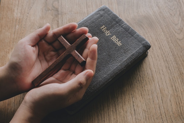 Mulher com uma cruz de madeira nas mãos, rezando pela bênção de Deus no antigo livro da Bíblia