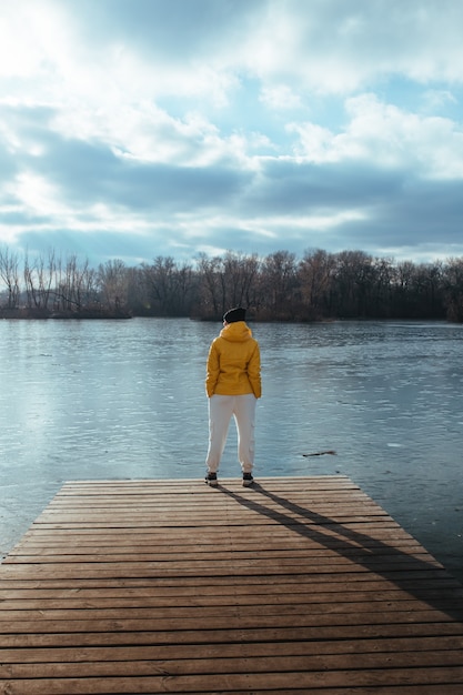 Mulher com uma jaqueta de inverno amarela contra um rio
