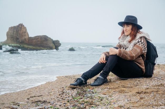 Mulher com uma mochila sentada na costa contra um fundo de rochas contra um lindo mar