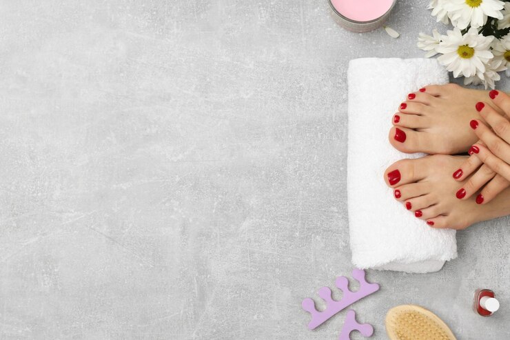 Foto mulher com unhas vermelhas elegantes depois de pedicura ferramentas de procedimento e flores de camomila em fundo de textura cinza vista superior espaço para texto