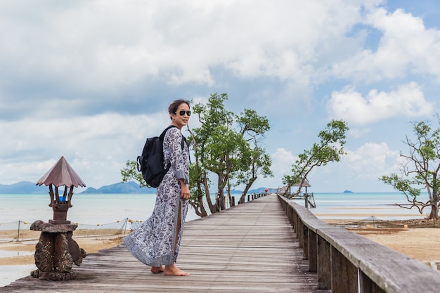 Mulher com vestido de verão em pé na ponte de madeira com vista do mar pacífica.