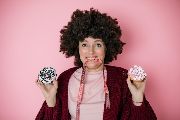 Mulher com vício em alimentos pastéis fica no fundo rosa e segura donuts. dependência alimentar, dieta alimentar. foto de humor, imposição de padrões de beleza.