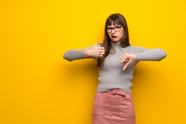 Mulher com vidros sobre a parede amarela que faz o sinal bom-mau. indeciso entre sim ou não