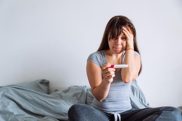Mulher com visão preocupada olhando para o teste de gravidez enquanto está sentado na cama