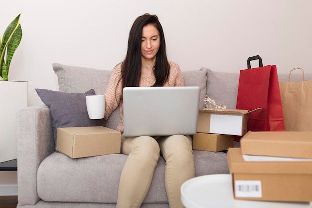 Mulher com vista frontal sentada no sofá enquanto verifica o laptop