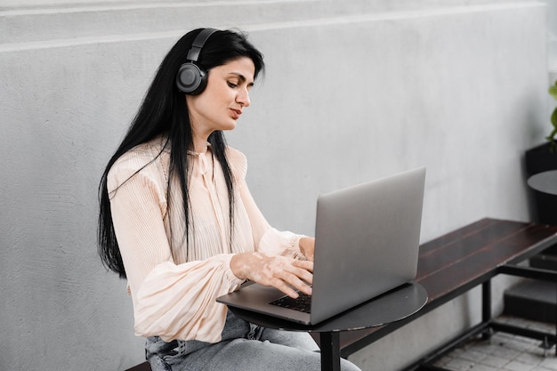 Mulher com vitiligo ouve música em fones de ouvido e trabalhando em laptop em cafée ao ar livre Mãos com pigmentação da pele com vitiligo Estilo de vida com doença sazonal da pele