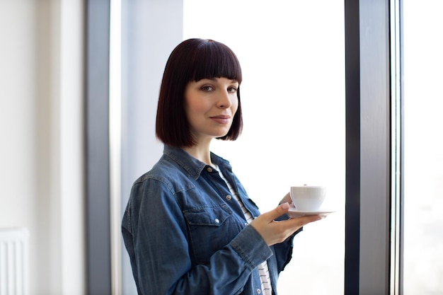 Mulher com xícara de café apreciando a vista da janela panorâmica