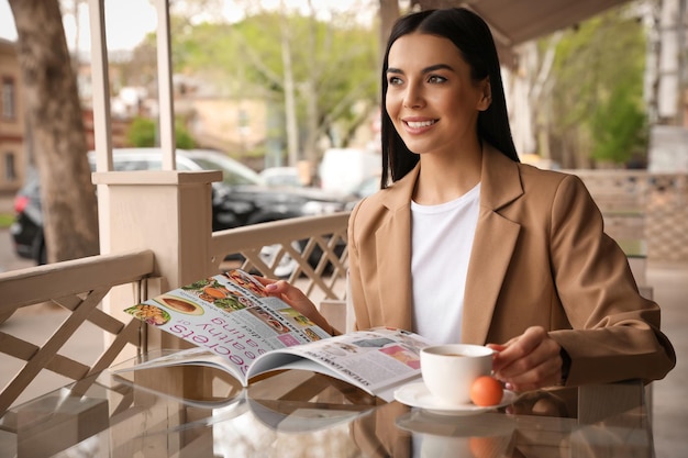 Mulher com xícara de café lendo revista no café ao ar livre na manhã