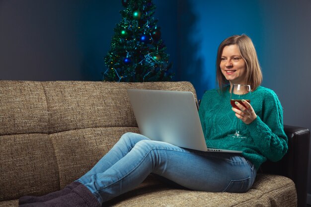 Mulher comemorando a véspera de natal com parentes por meio de uma chamada on-line no laptop com uma taça de vinho