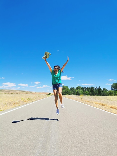 Foto mulher comemorando correndo pulando pulando e brincando em uma estrada solitária