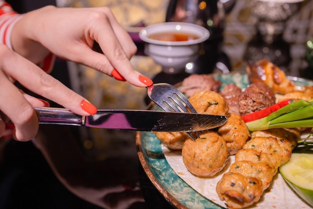 Mulher comendo churrasco em um café com as mãos femininas fechadas segurando um garfo com um pedaço de churrasco