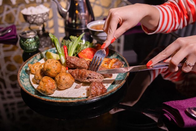 Mulher comendo churrasco em um café com as mãos femininas fechadas segurando um garfo com um pedaço de churrasco