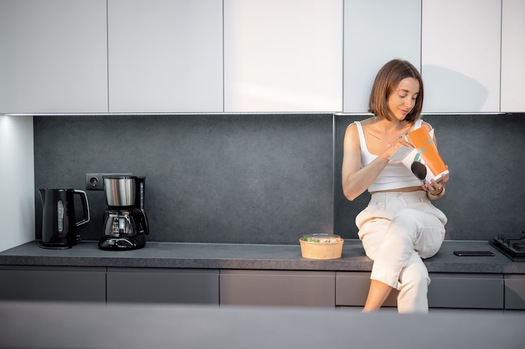 Foto mulher comendo comida para viagem sentada na cozinha moderna
