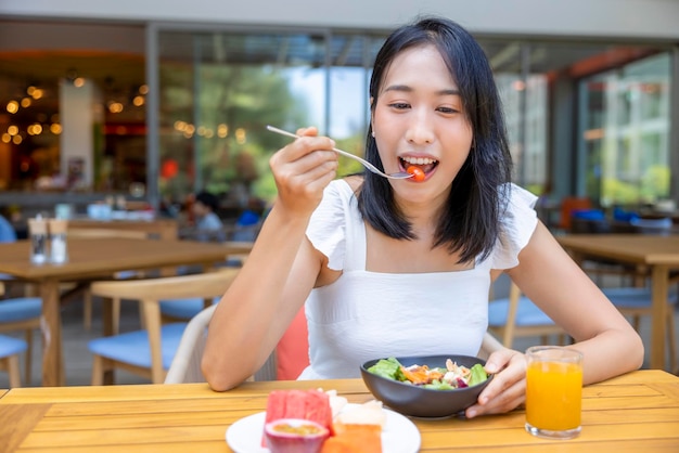 Mulher comendo frutas do café da manhã, como melancia, mamão, melão, maracujá, suco de laranja e café, colocado em um tapete cinza