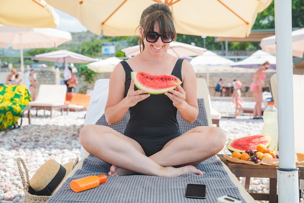 Mulher comendo frutas na praia. férias de verão. espreguiçadeira