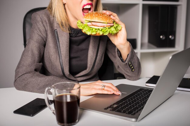 Mulher comendo hambúrguer enquanto trabalhava