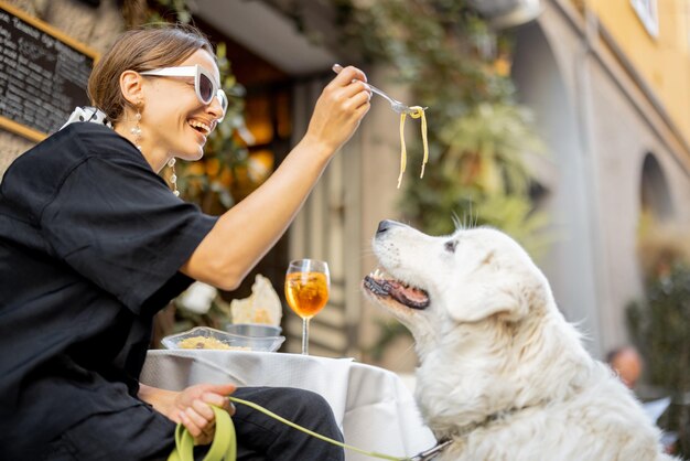 Mulher comendo macarrão com seu cachorro branco fofo no restaurante