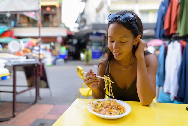 Mulher comendo macarrão pad thai na estrada khao san