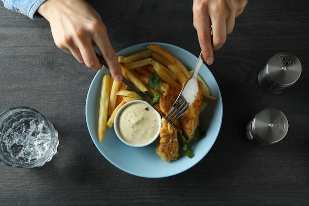 Mulher comendo peixe frito com batatas fritas na mesa escura