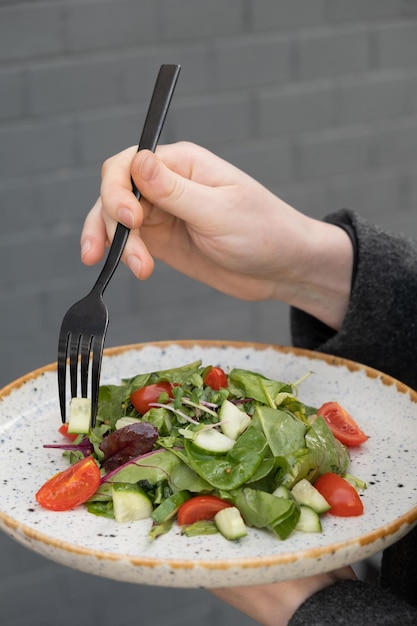 Mulher comendo salada fresca com rúcula, tomates, pepinos em um close de prato