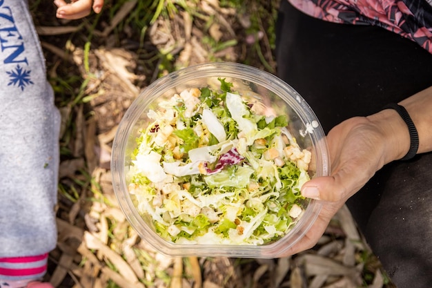 Mulher comendo salada no campo em recipiente de plástico