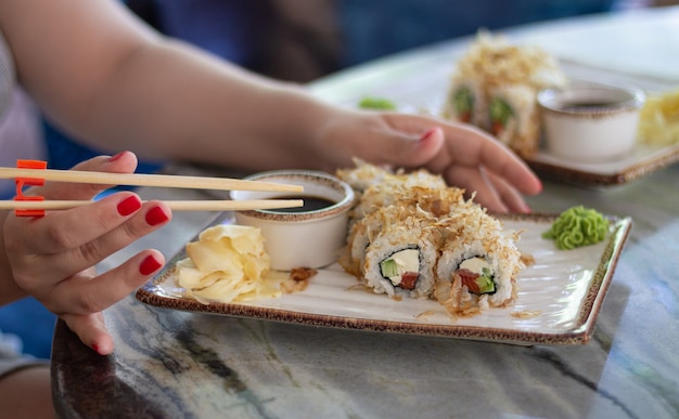 Mulher comendo sushi com molho de soja, wasabi e palitos em restaurante