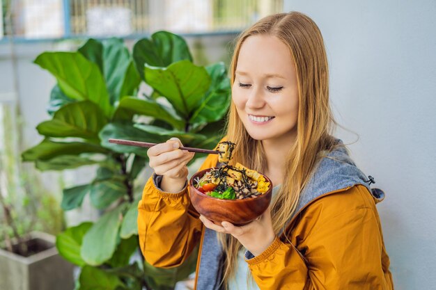 Mulher comendo tigela de poke orgânica crua com arroz e legumes closeup na mesa vista de cima