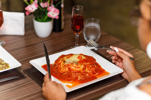 Mulher comendo um delicioso prato de carne e macarrão à parmegiana.