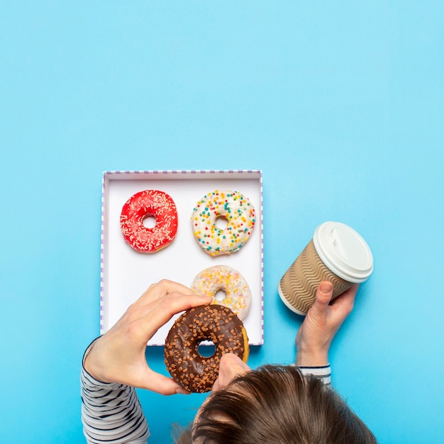 Mulher comendo uma rosquinha e bebendo café em um azul. confeitaria conceito, pastelaria, cafetaria