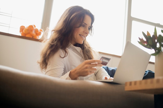 Mulher compras on-line no laptop no sofá com cartão de crédito