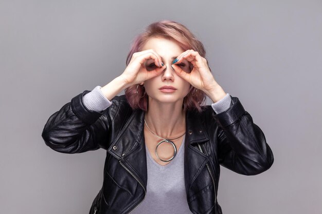 Mulher concentrada atenta com penteado curto em pé fazendo gesto binocular