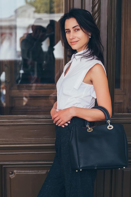 Foto mulher confiante com bolsa preta apoiada em uma porta de madeira