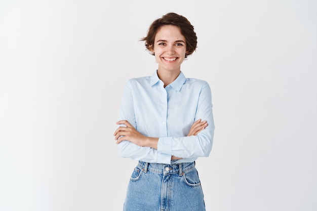 Mulher confiante do escritório, usando uma camisa azul, cruze os braços no peito e uma parede branca sorridente