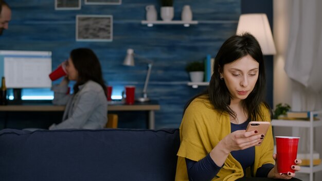 Mulher confiante lendo notificação de e-mail usando smartphone enquanto relaxa no sofá tarde da noite em ...