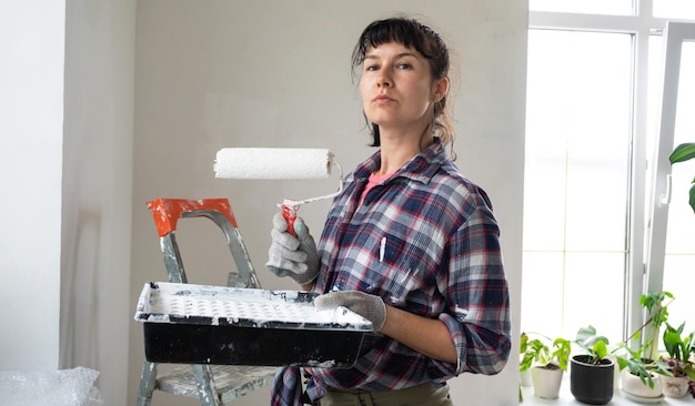 Mulher confusa em rolo de pintura e tinta branca para paredes em retrato de closeup de mãos trabalhos de construção e reparos cosméticos em pintura de parede de casa, acabamento de acabamento com suas próprias mãos