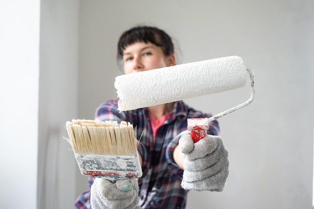 Mulher confusa em rolo de pintura e tinta branca para paredes em retrato de closeup de mãos Trabalhos de construção e reparos cosméticos em pintura de parede de casa, acabamento de acabamento com suas próprias mãos