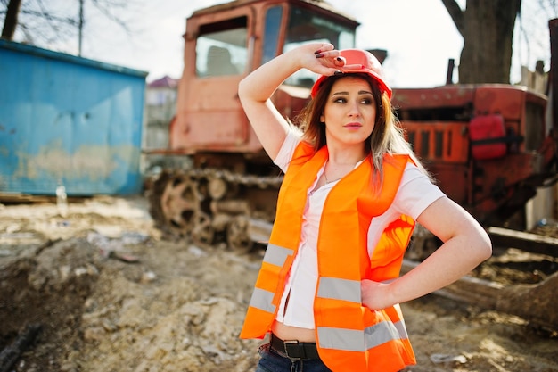 Mulher construtor engenheiro em colete uniforme e capacete protetor laranja contra bulldozer