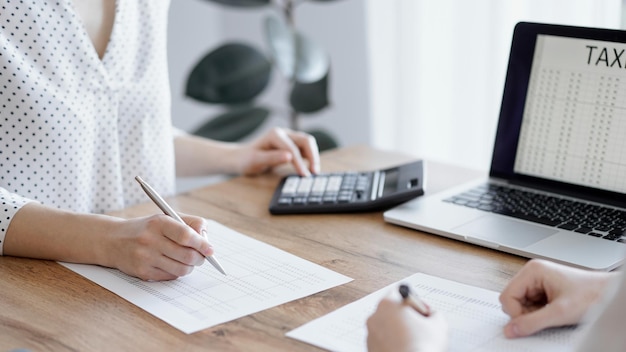 Mulher contadora usando uma calculadora e um laptop enquanto contava impostos com um colega na mesa de madeira no escritório Trabalho em equipe em auditoria de negócios e finanças.