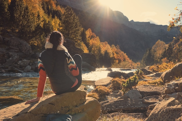 Mulher contemplando a correnteza de um rio iluminado pela luz do sol entre as montanhas. Pôr do sol na floresta no outono. Parque Natural Ordesa y Monte Perdido nos Pirineus